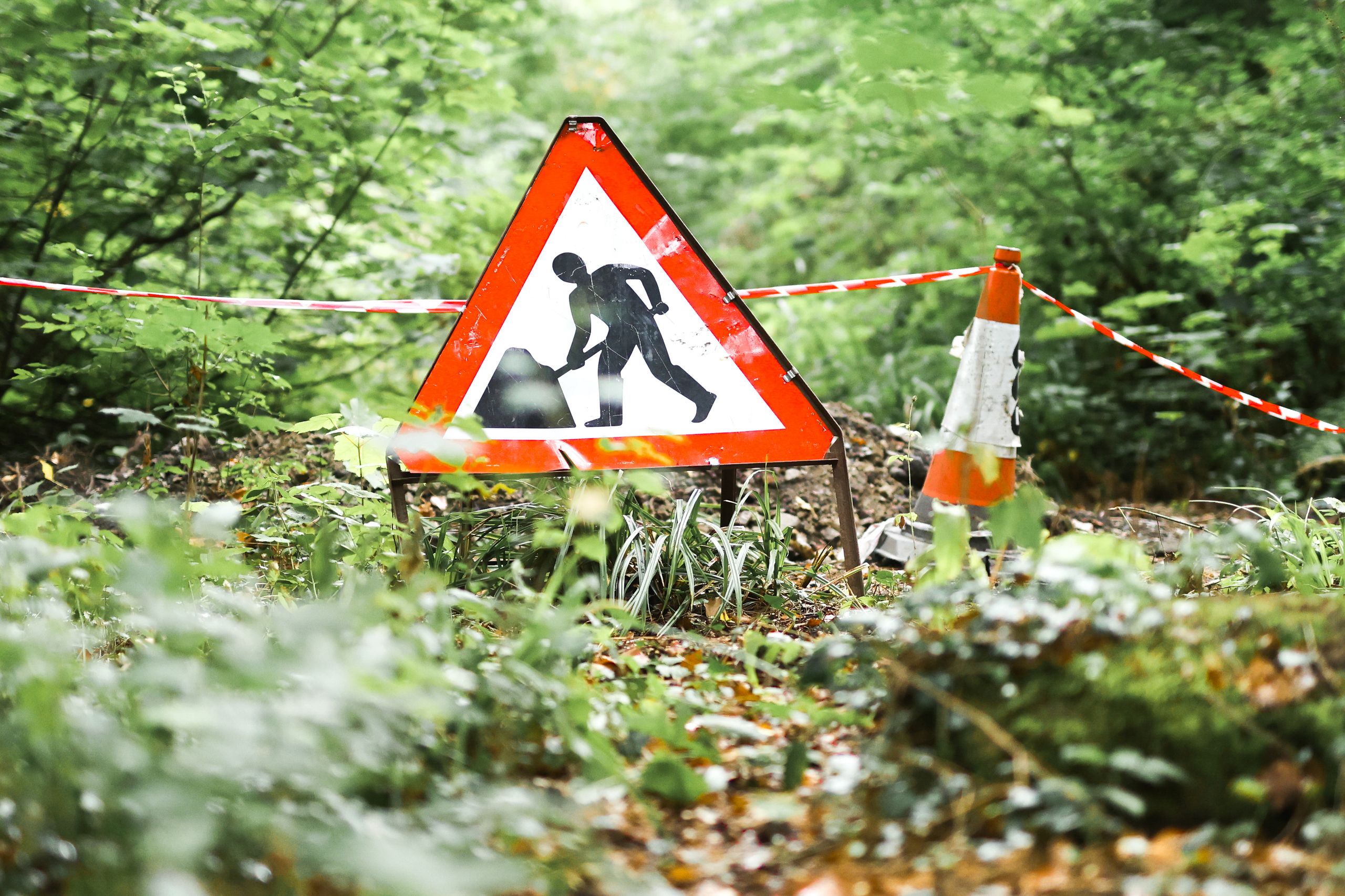 A road work sign in a forest setting in Ironbridge, UK, indicating an ongoing construction project amidst lush surroundings.